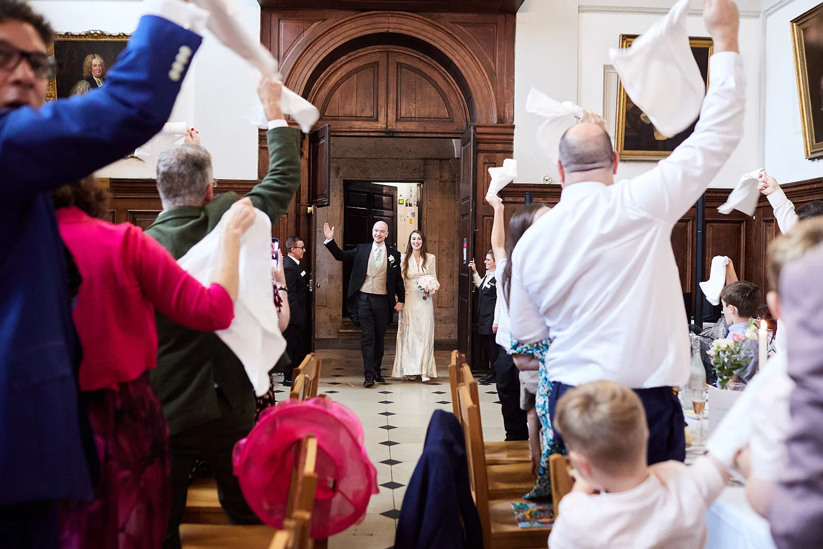 Newlyweds enter the reception hall hand in hand as enthusiastic guests wave their white napkins in the air to celebrate.