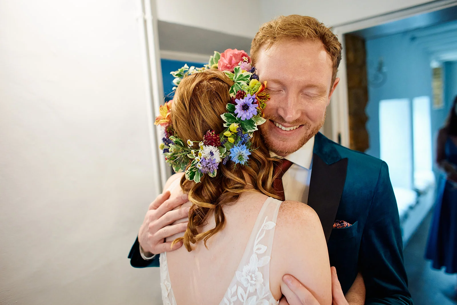A smiling groom embraces a bride wearing a vibrant floral crown and a detailed gown.