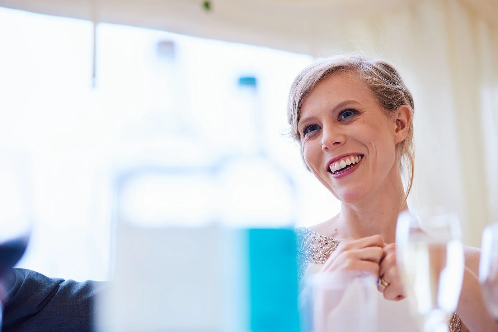 A joyful bride laughs happily during the wedding breakfast, captured in soft window light with a shallow depth of field.