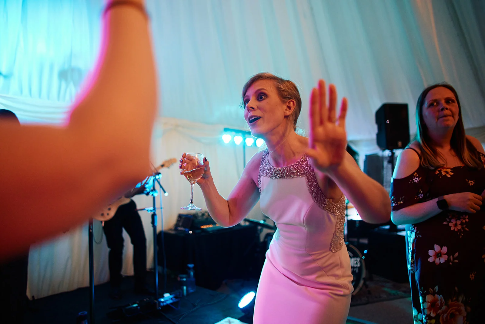 A guest holding a drink dances excitedly on the illuminated dance floor inside a marquee wedding reception.