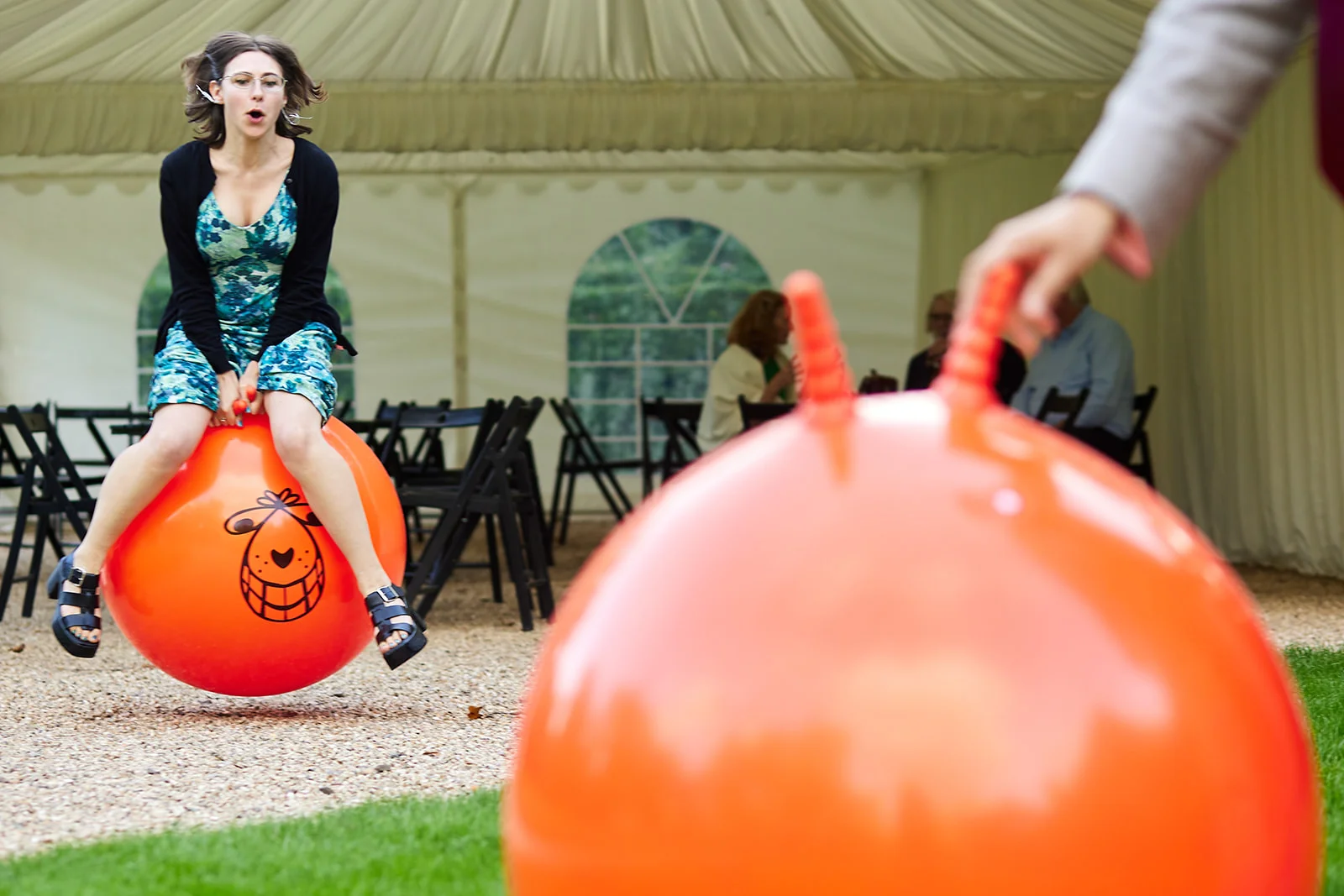 A wedding guest joyfully bounces on a large orange space hopper outside a marquee during the wedding reception.