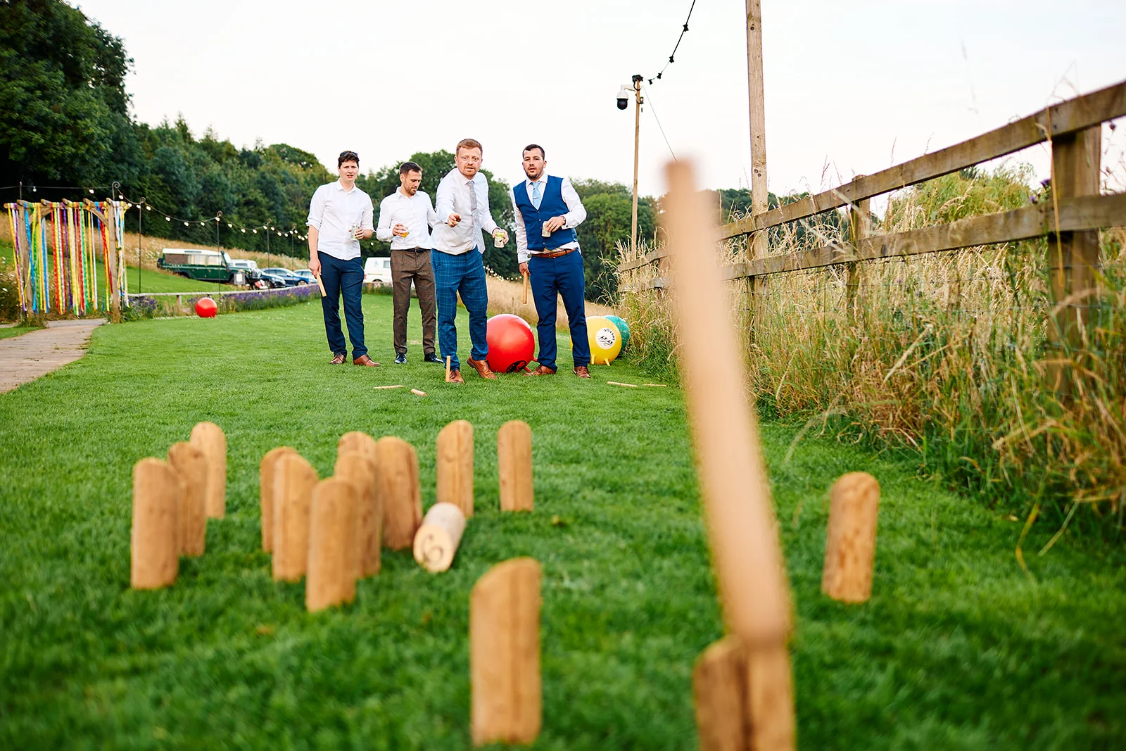 Four groomsmen play a game of wooden skittles on the lawn during an outdoor wedding reception in the countryside.