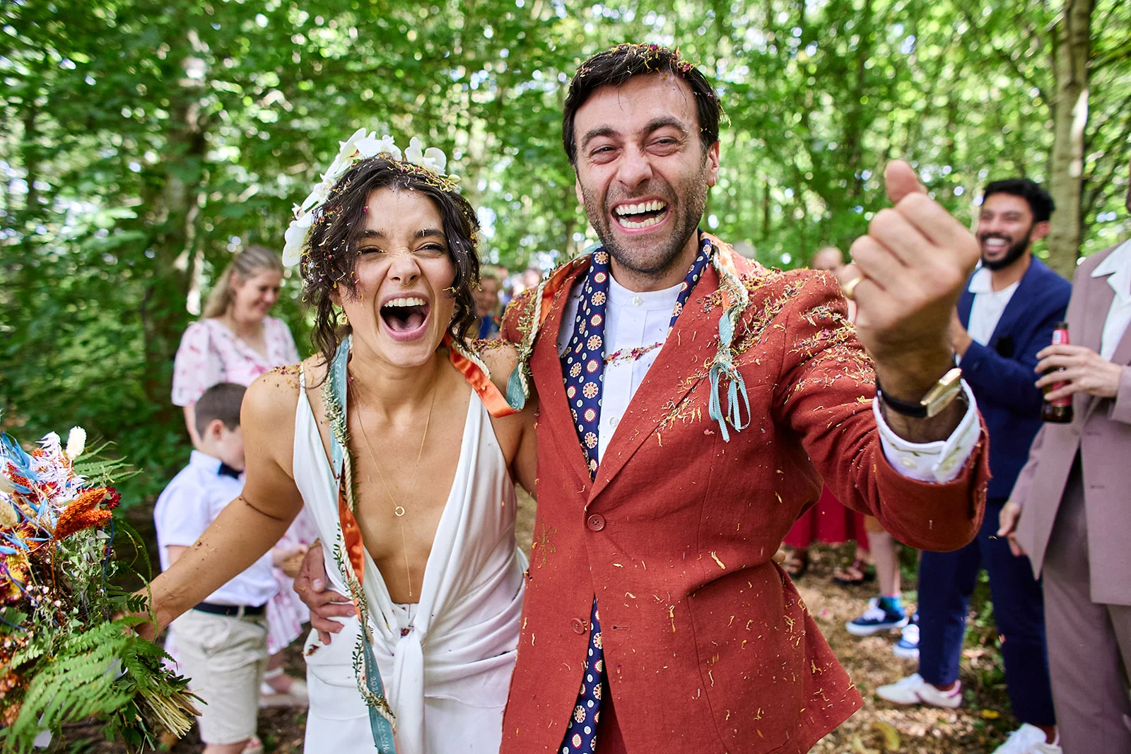 A joyous bride and groom laugh ecstatically as confetti rains down on them during their outdoor woodland wedding celebration.