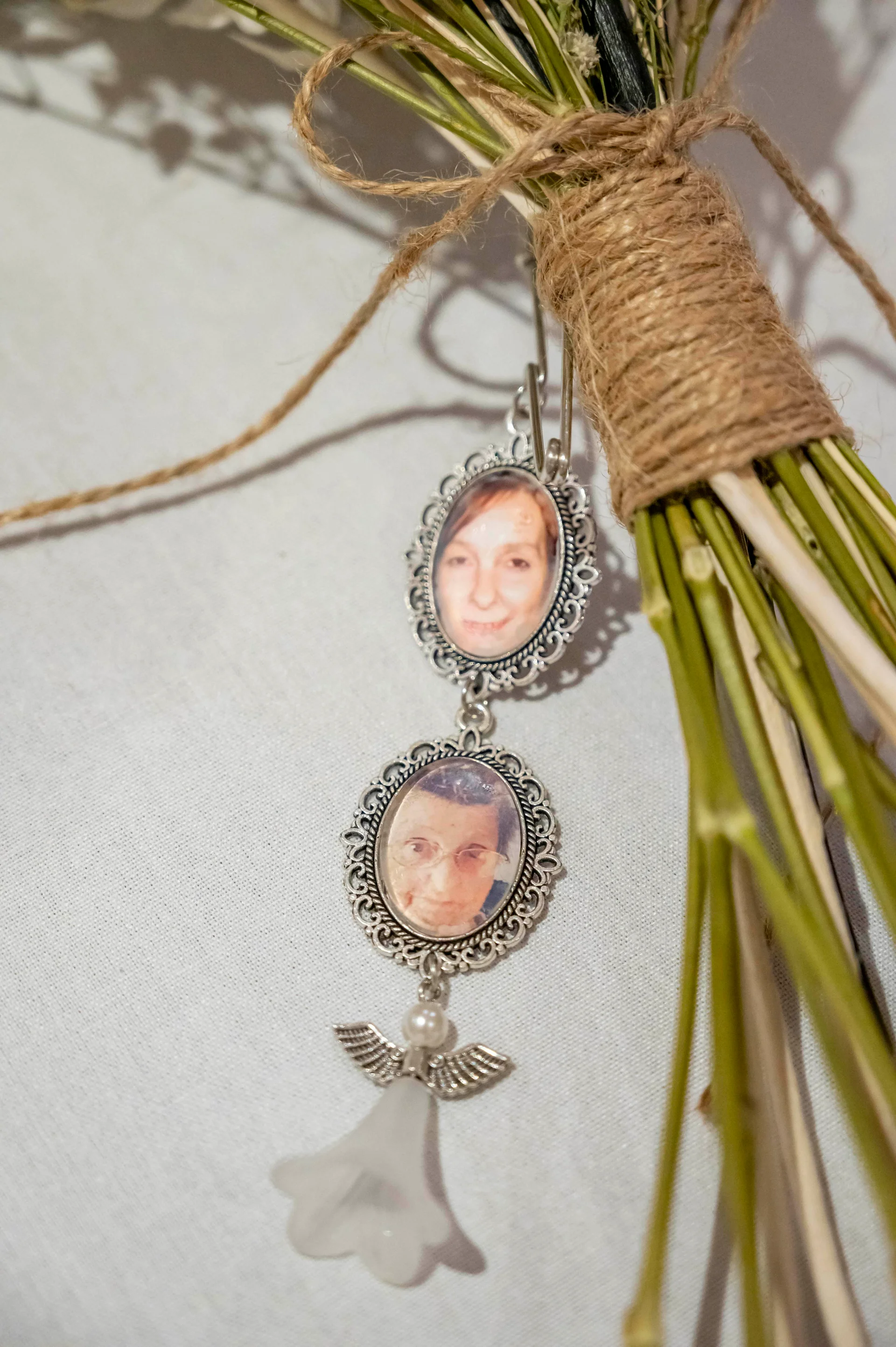 A close-up detail shot shows a rustic twine-wrapped bouquet stem adorned with a double silver photo locket and memorial angel charm.