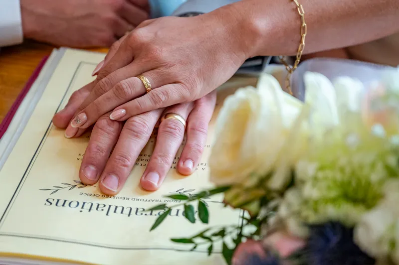 The newlywed couple proudly display their wedding bands while resting their hands on top of the marriage certificate during the ceremony.