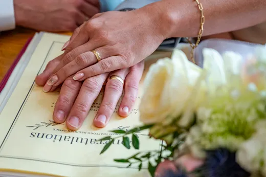The newlywed couple proudly display their wedding bands while resting their hands on top of the marriage certificate during the ceremony.