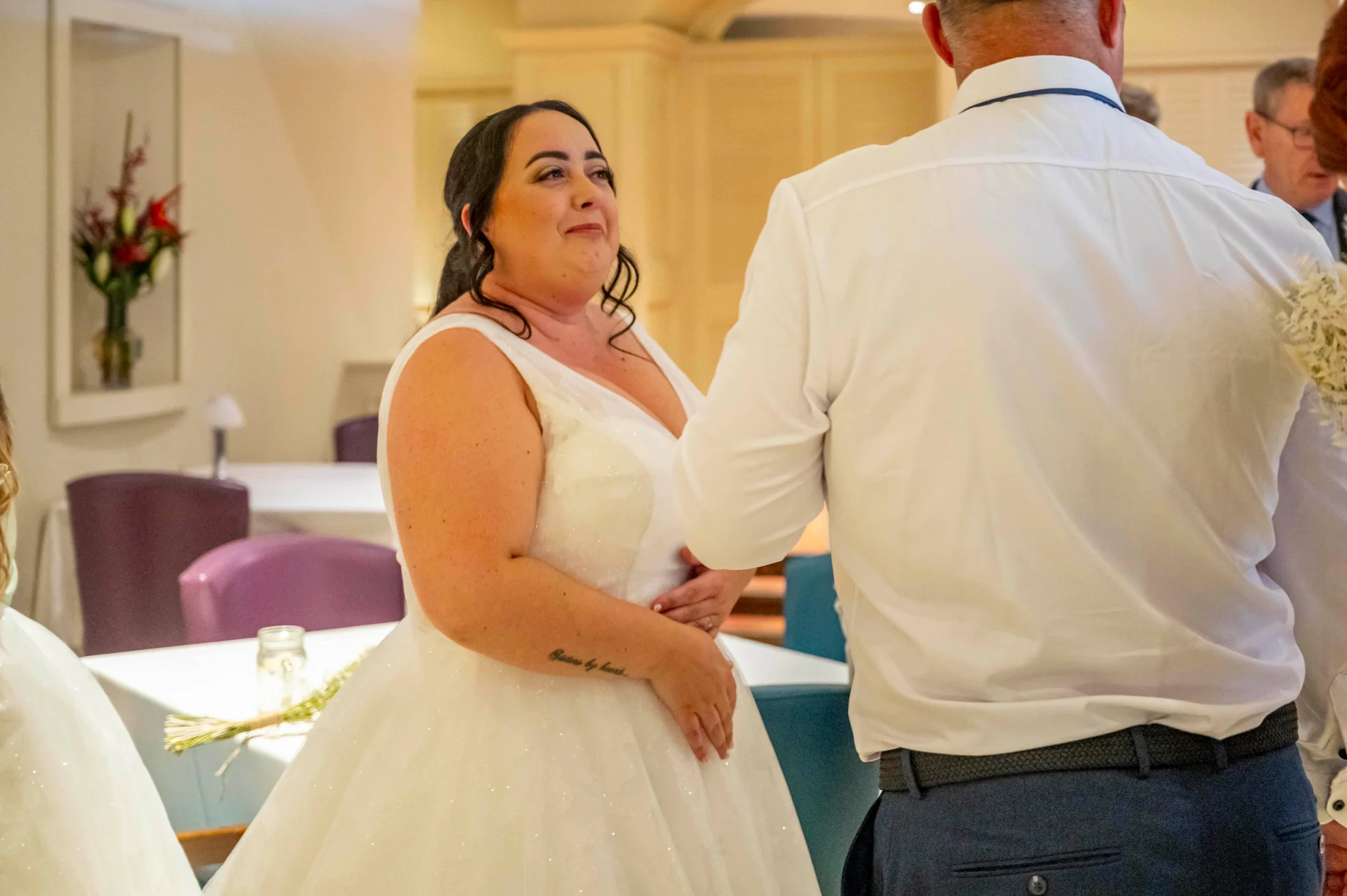 An emotional plus size bride wearing a white glittery gown with a v-neckline laughs as she interacts with guests during the reception.