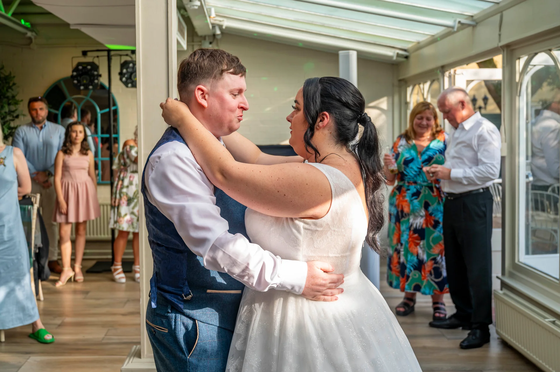 Newlyweds share their first dance together inside a bright conservatory venue surrounded by family and guests.