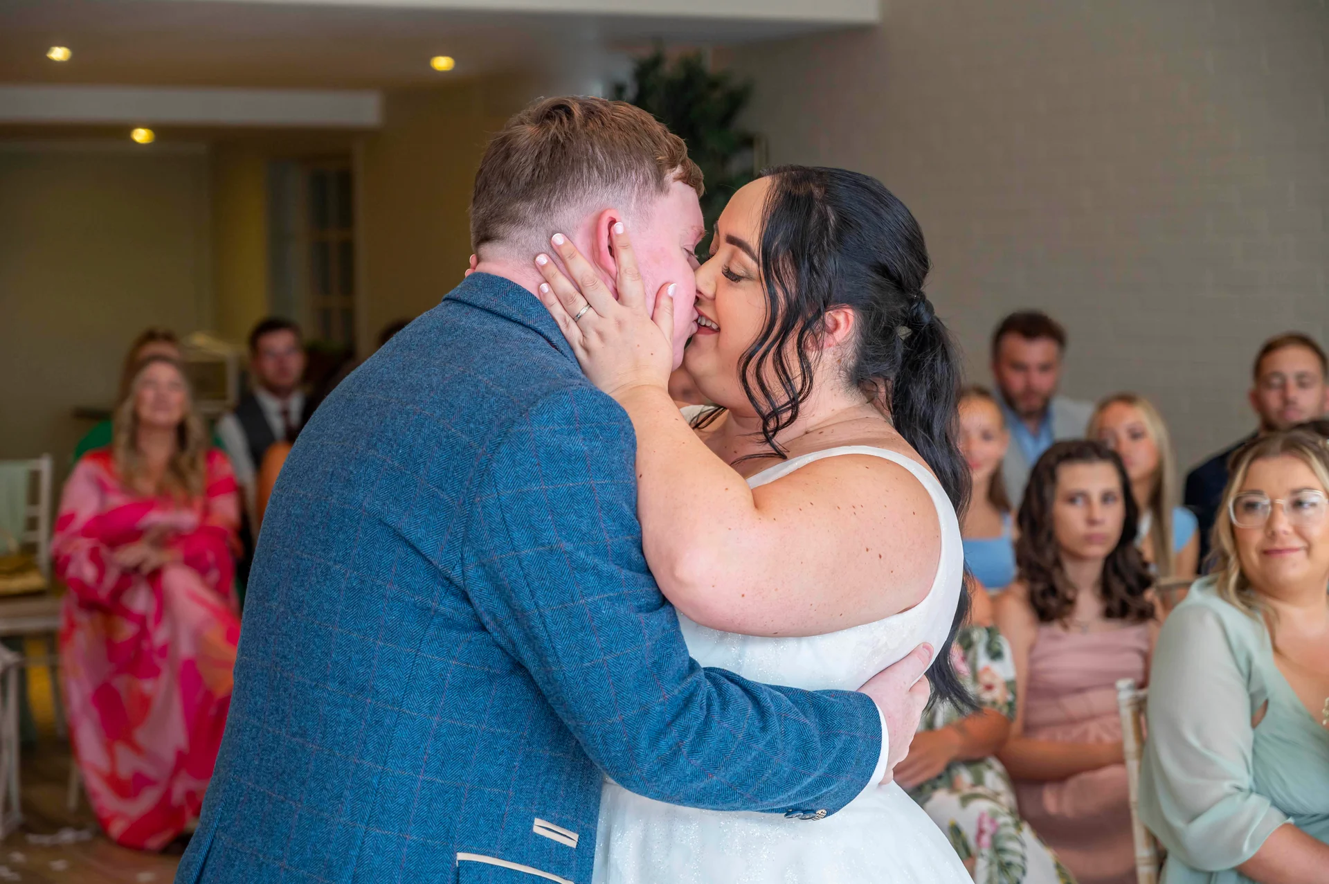 Newlyweds share an emotional first kiss during their civil ceremony as seated guests look on happily.
