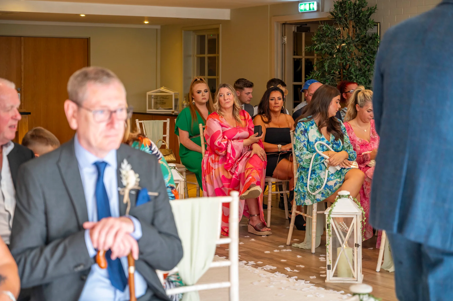 A candid view of wedding guests seated along an aisle scattered with petals as they watch the ceremony unfold indoors.