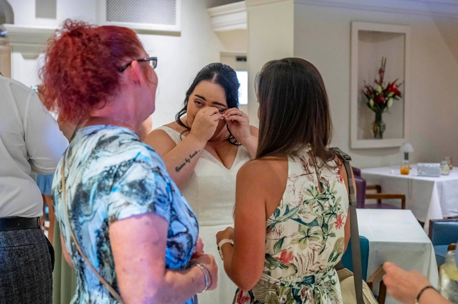 An emotional bride wipes away happy tears while conversing with wedding guests during the reception.