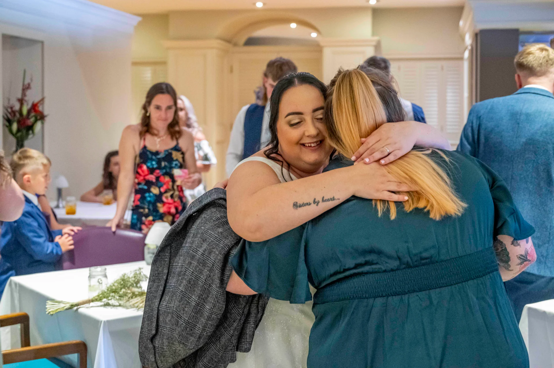 A smiling bride shares a warm, emotional embrace with a wedding guest during the reception celebration.