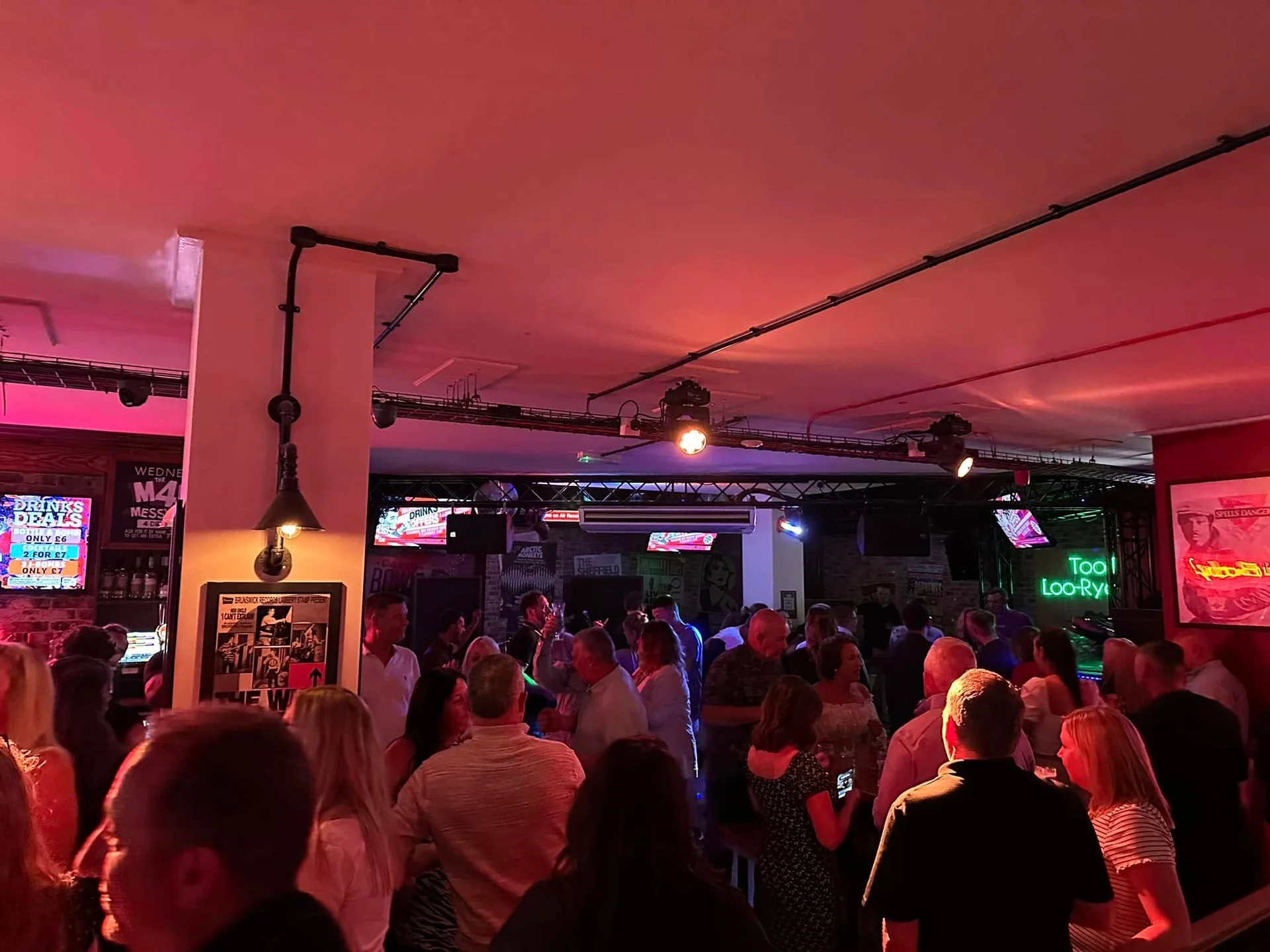 Wedding guests mingle and enjoy the evening reception inside a lively pub illuminated by ambient red and theatrical lighting.