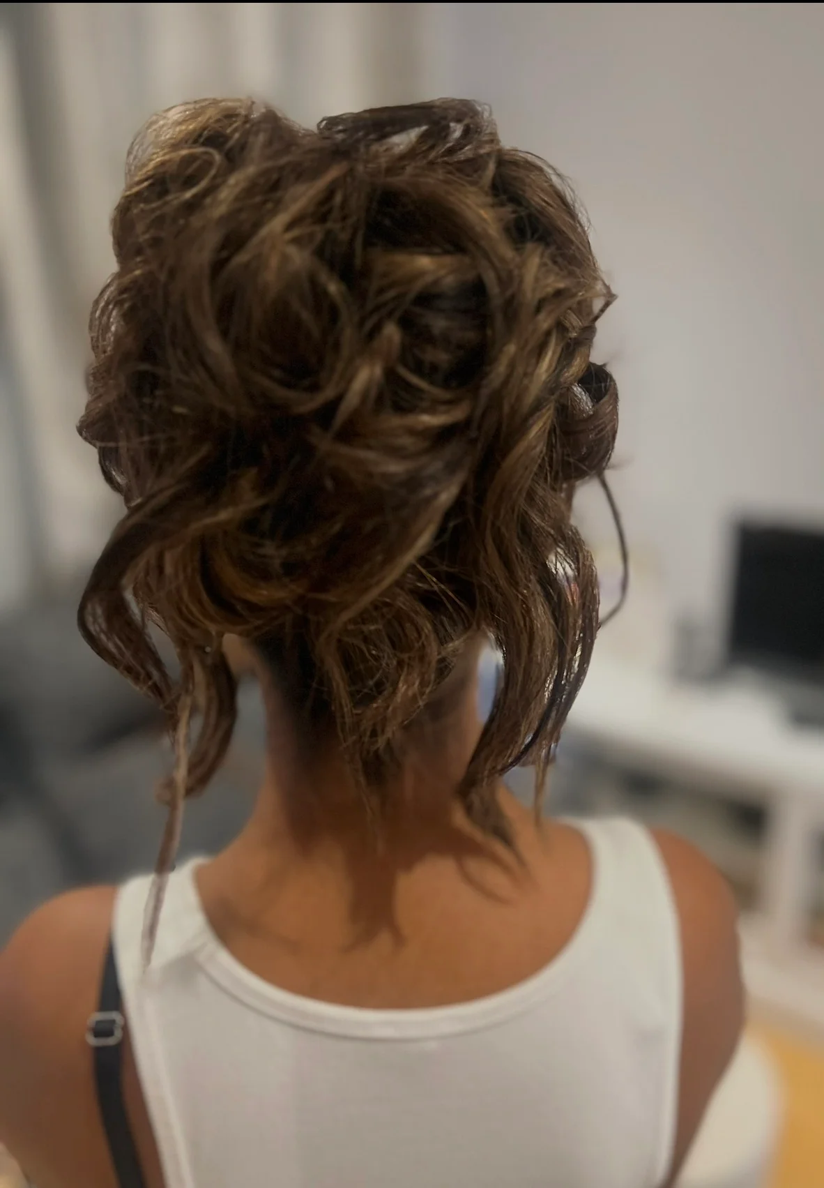A close-up back view of a bride showcasing an intricate, textured updo with soft, romantic curls framing her neck during bridal preparation.