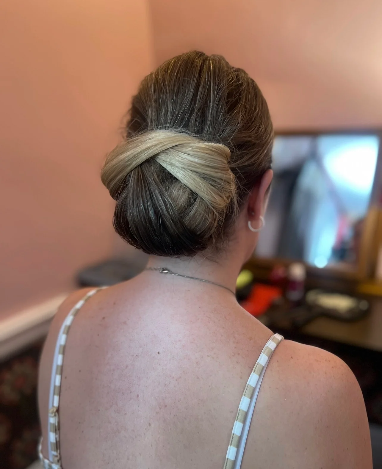 A detailed back view of a bride showcasing an intricate low chignon hairstyle with highlighted hair during morning preparations.