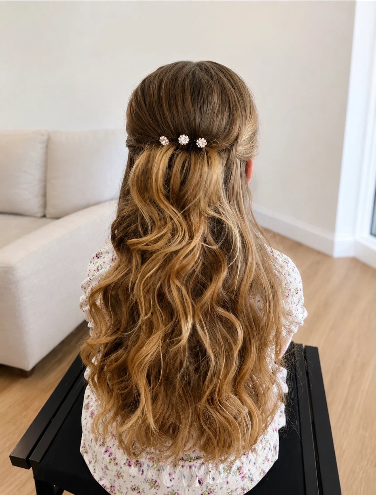 A back view of a person with long, flowing brown hair styled in soft waves in a half-up half-down look secured with sparkling decorative hair pins.