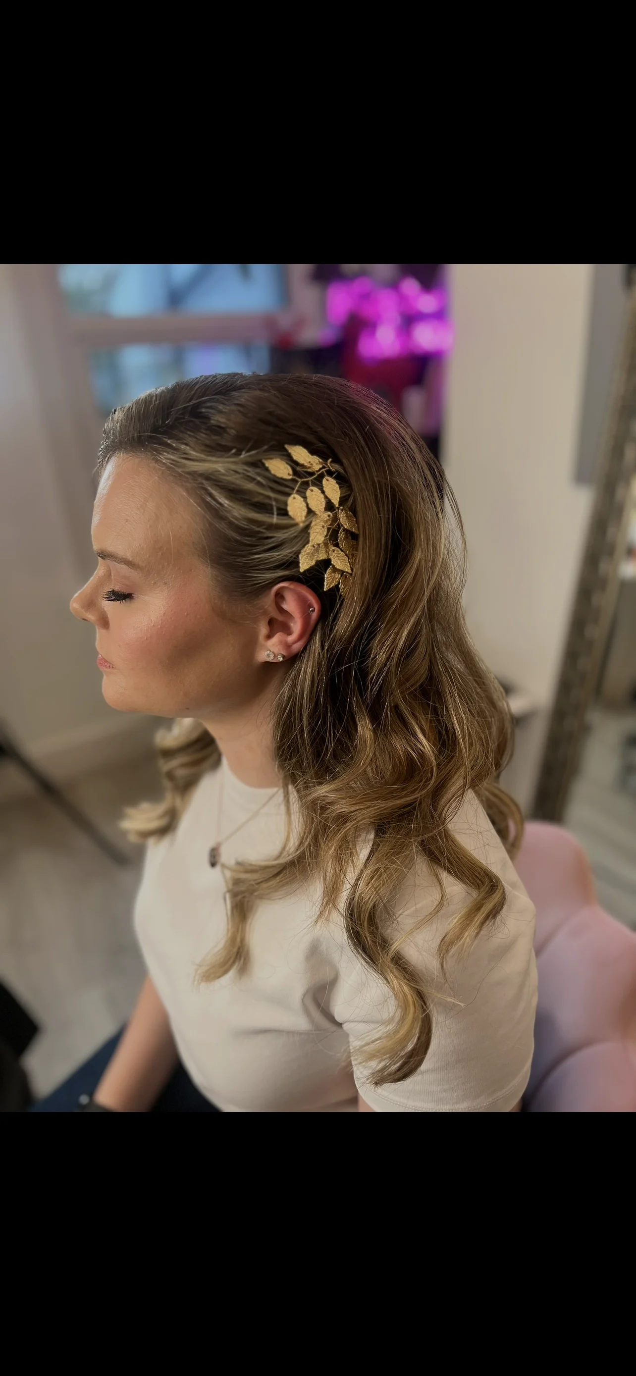 A profile view of a bride with long wavy hair adorned with an intricate gold leaf hair comb during her wedding morning preparation.