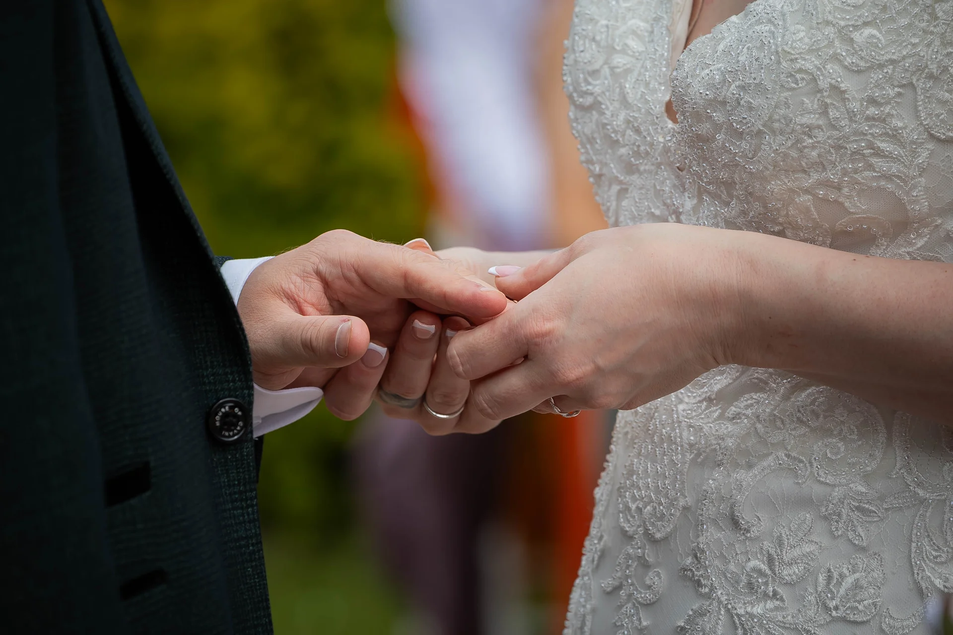 A close-up shot captures the tender moment during the ceremony as the bride and groom exchange rings, highlighting the intricate lace detail of her wedding gown.