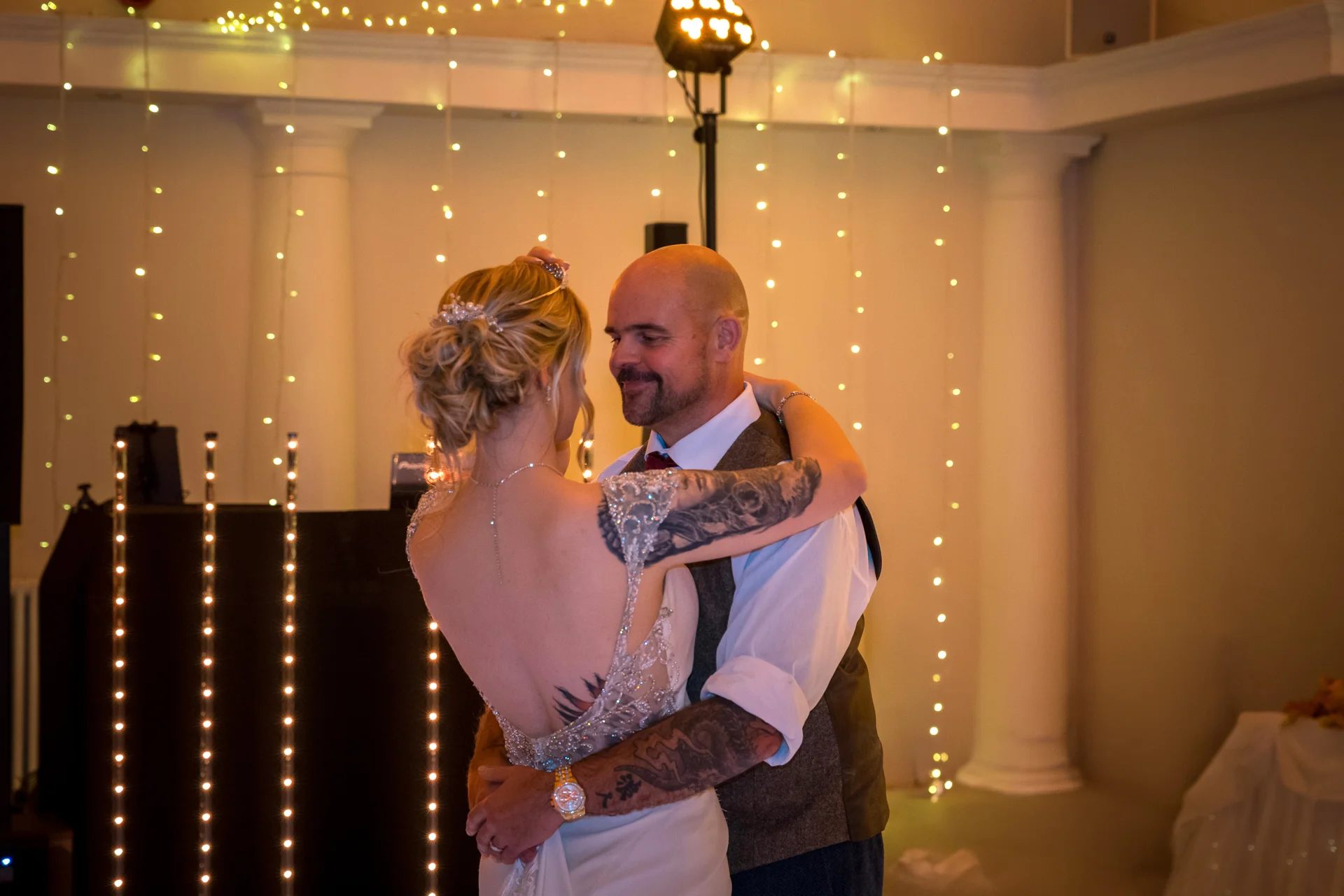 A newlywed couple shares their first dance during the evening reception, surrounded by twinkling fairy lights and subtle venue decor.