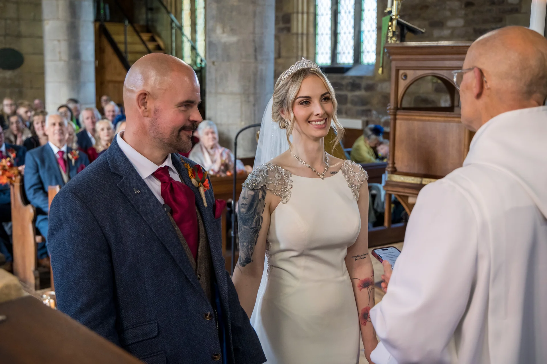 A smiling bride and groom stand together at the altar during their traditional church wedding ceremony, facing the officiant.