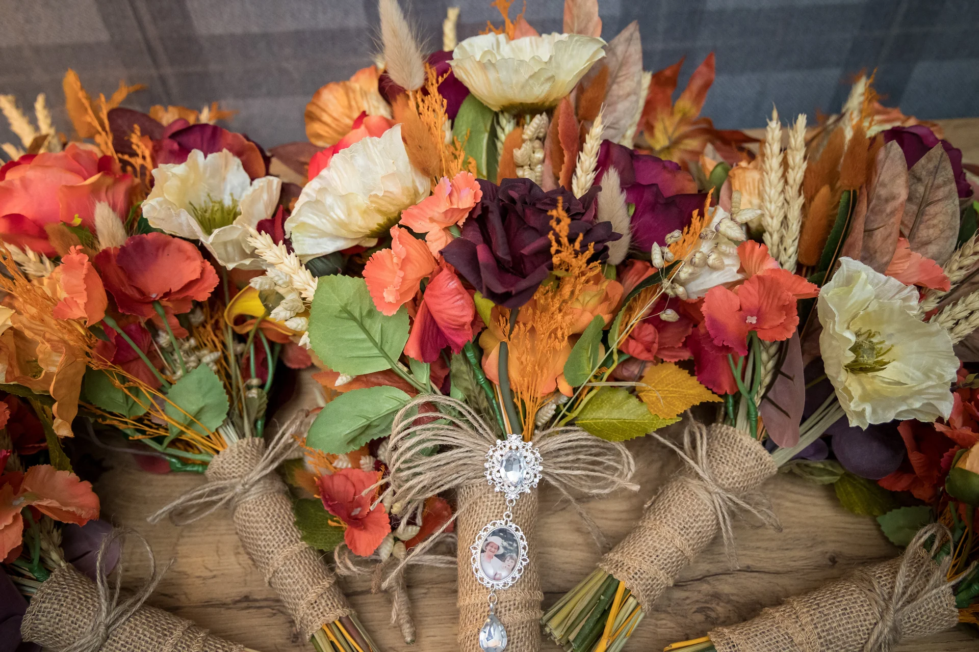 A collection of handmade autumnal wedding bouquets featuring terracotta, orange, cream, and deep burgundy blooms tied with hessian and twine charms.