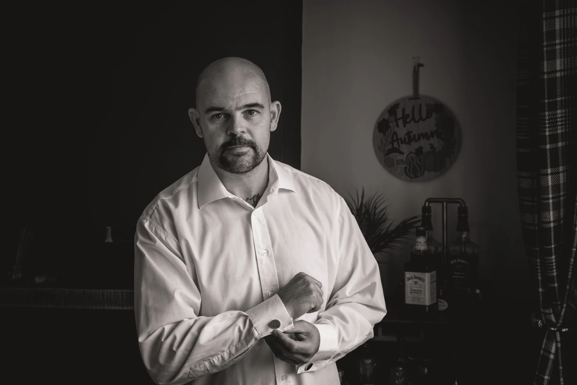 A groom adjusts his cufflinks while getting ready in a white button-down shirt for his wedding day.