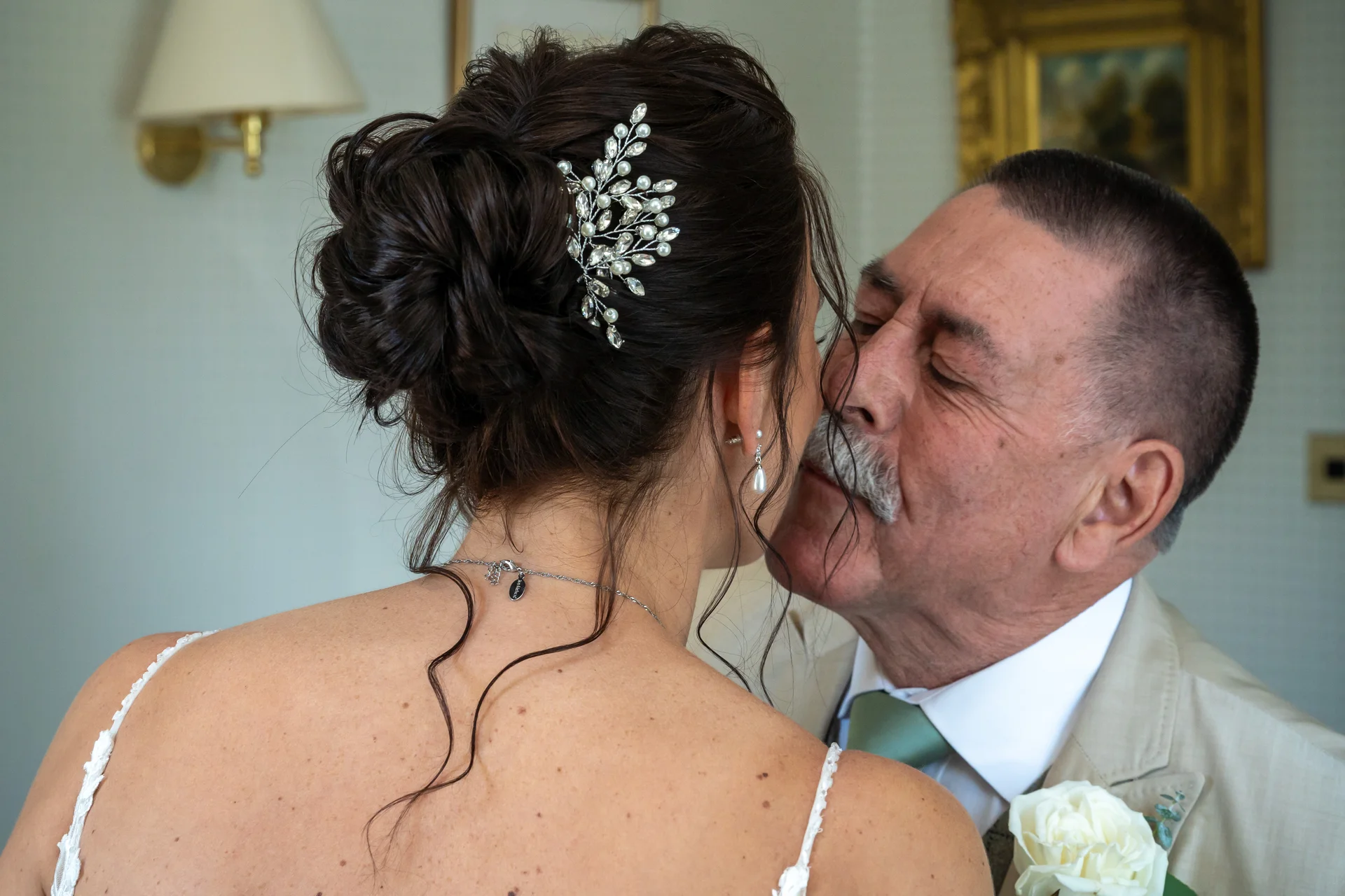 A father of the bride shares a tender, emotional moment with his daughter during bridal preparations, wearing a suit and a white rose boutonniere.