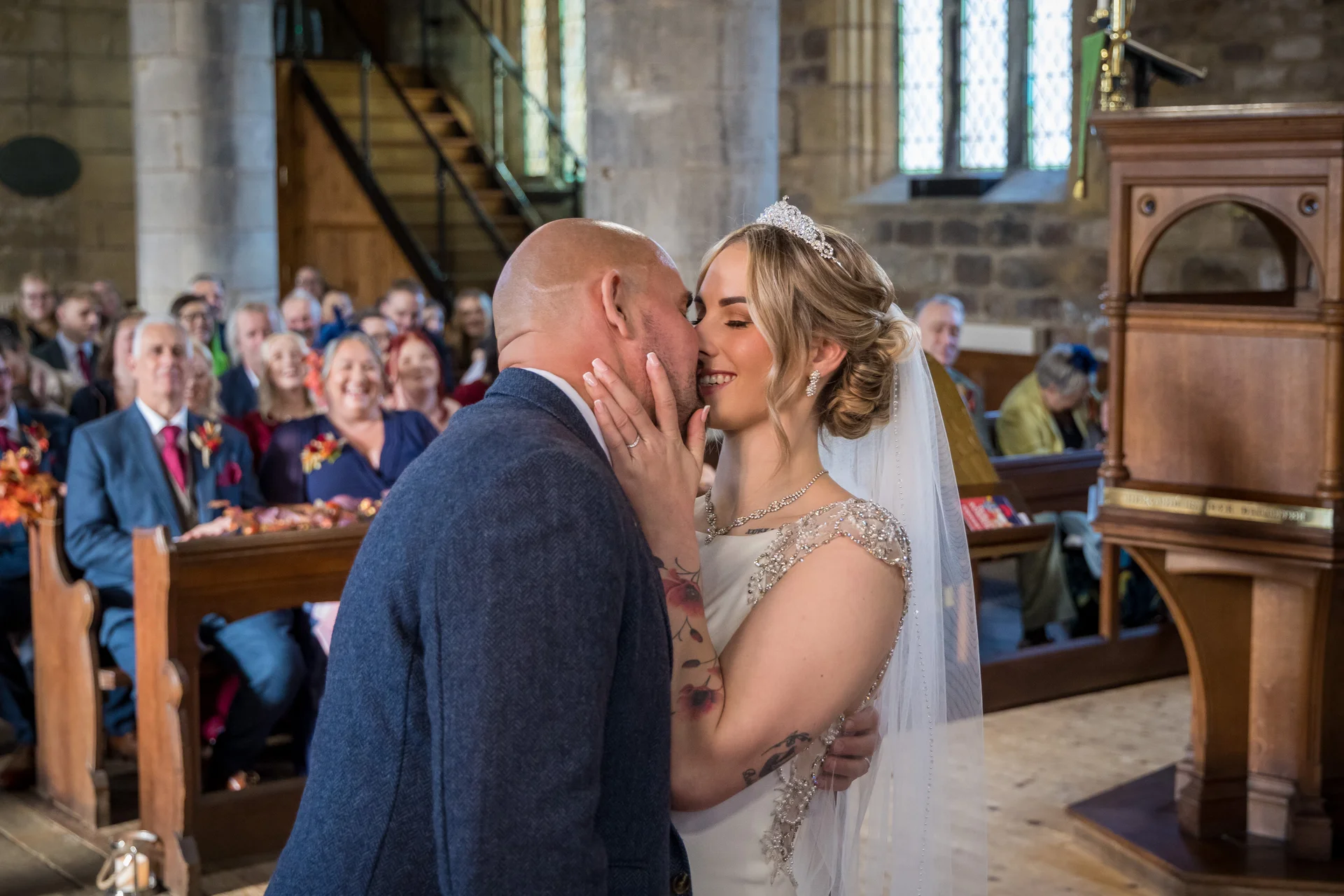Newlyweds share their first kiss at the altar during a traditional church wedding ceremony while guests watch from the pews.