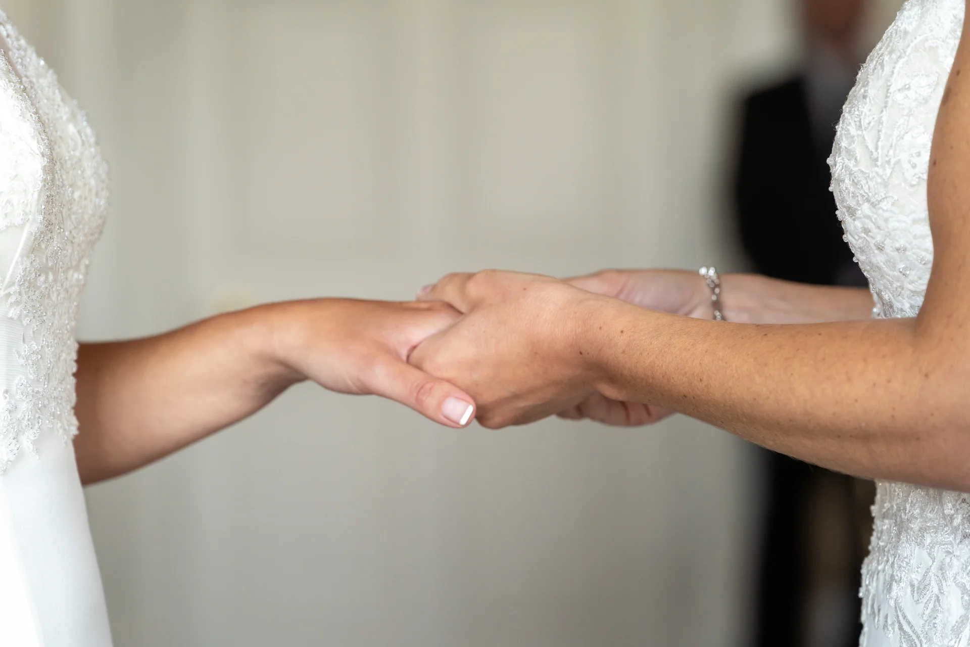 Two brides gently hold hands and exchange wedding bands during a heartfelt indoor ceremony.