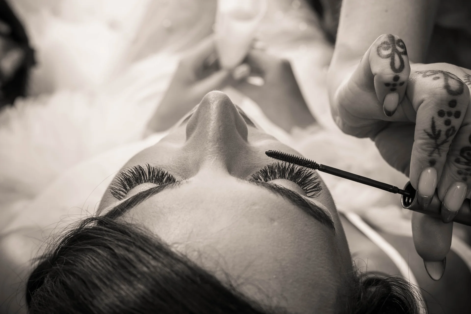 An extreme close up black and white shot captures a makeup artist applying mascara to a bride's long, dark lashes during wedding morning preparations.