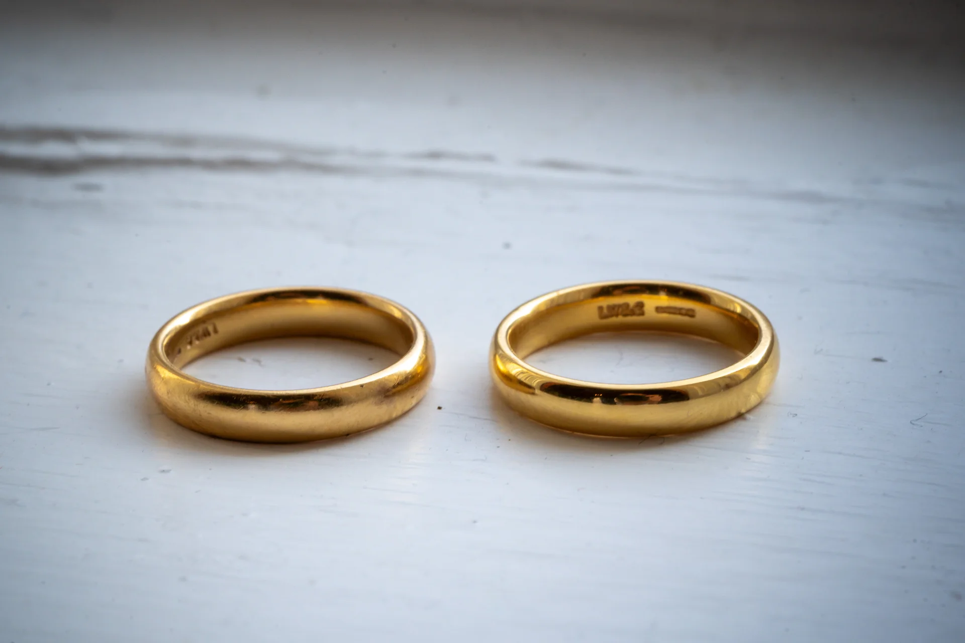 Two polished yellow gold wedding bands rest side by side on a textured white surface.