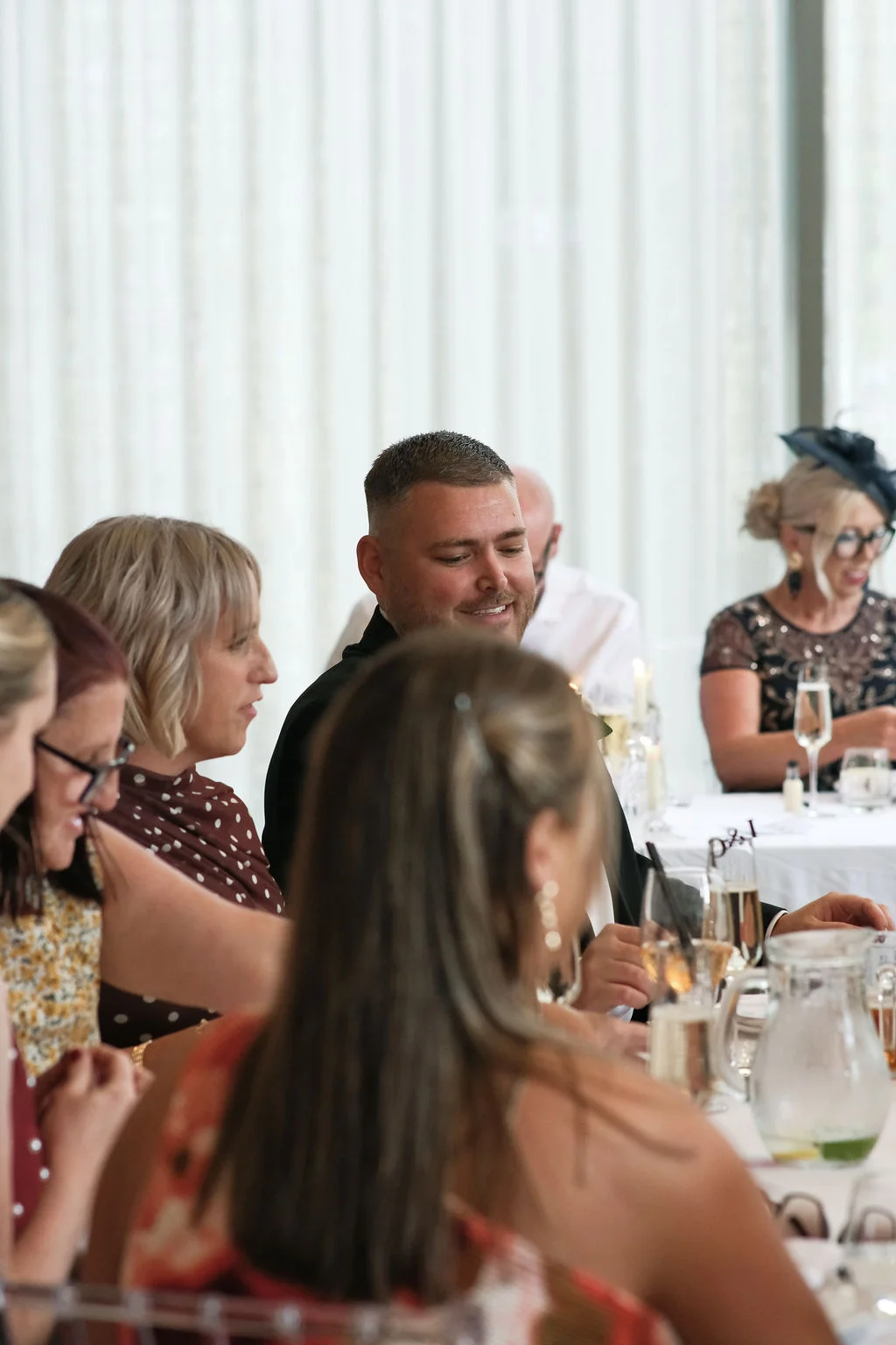 Wedding guests enjoy conversation seated at a long banquet table during the daytime reception.