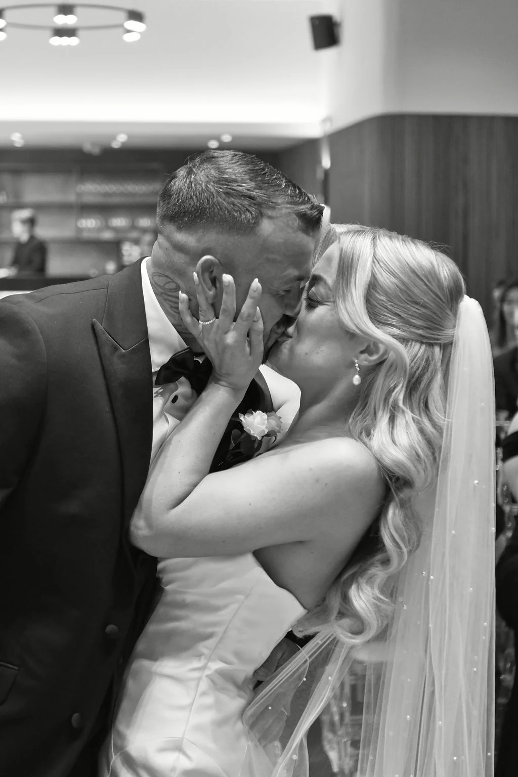 A bride and groom share a passionate dip kiss during their wedding celebration, captured in a striking black and white photograph.