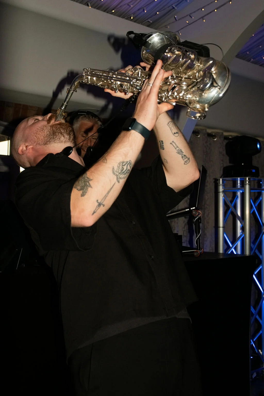 A tattooed saxophonist passionately plays his instrument on stage under dynamic blue lighting during a wedding evening reception.