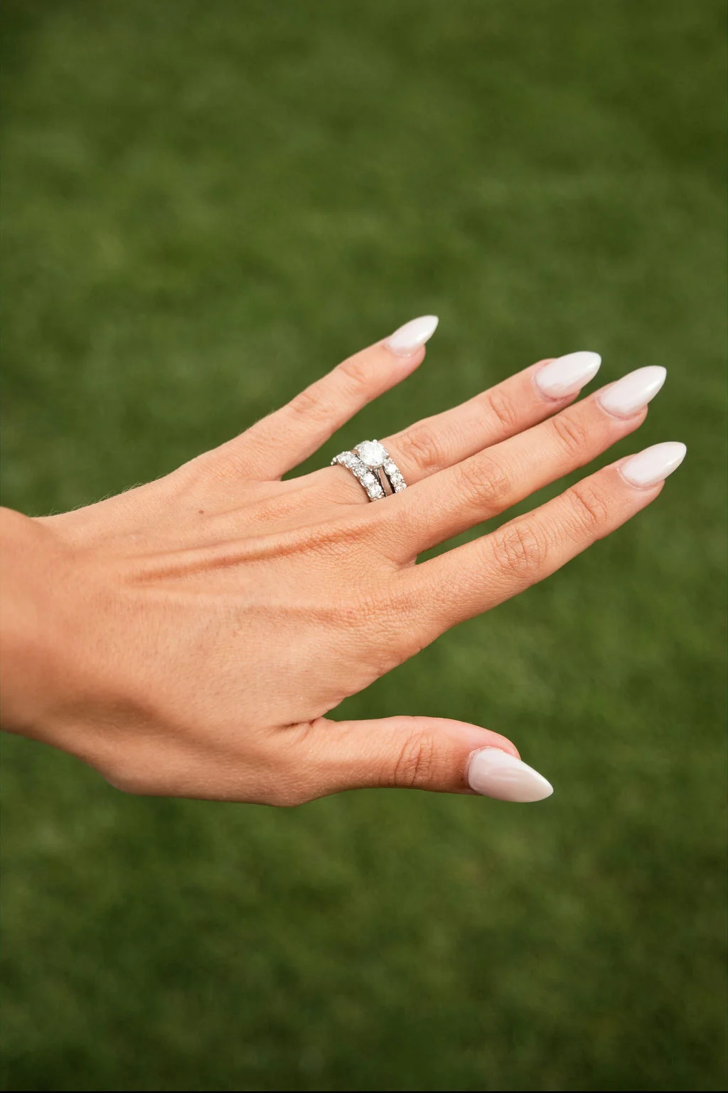 Close-up of a bride's hand showcasing a sparkling diamond engagement ring and matching wedding band against a soft green background.