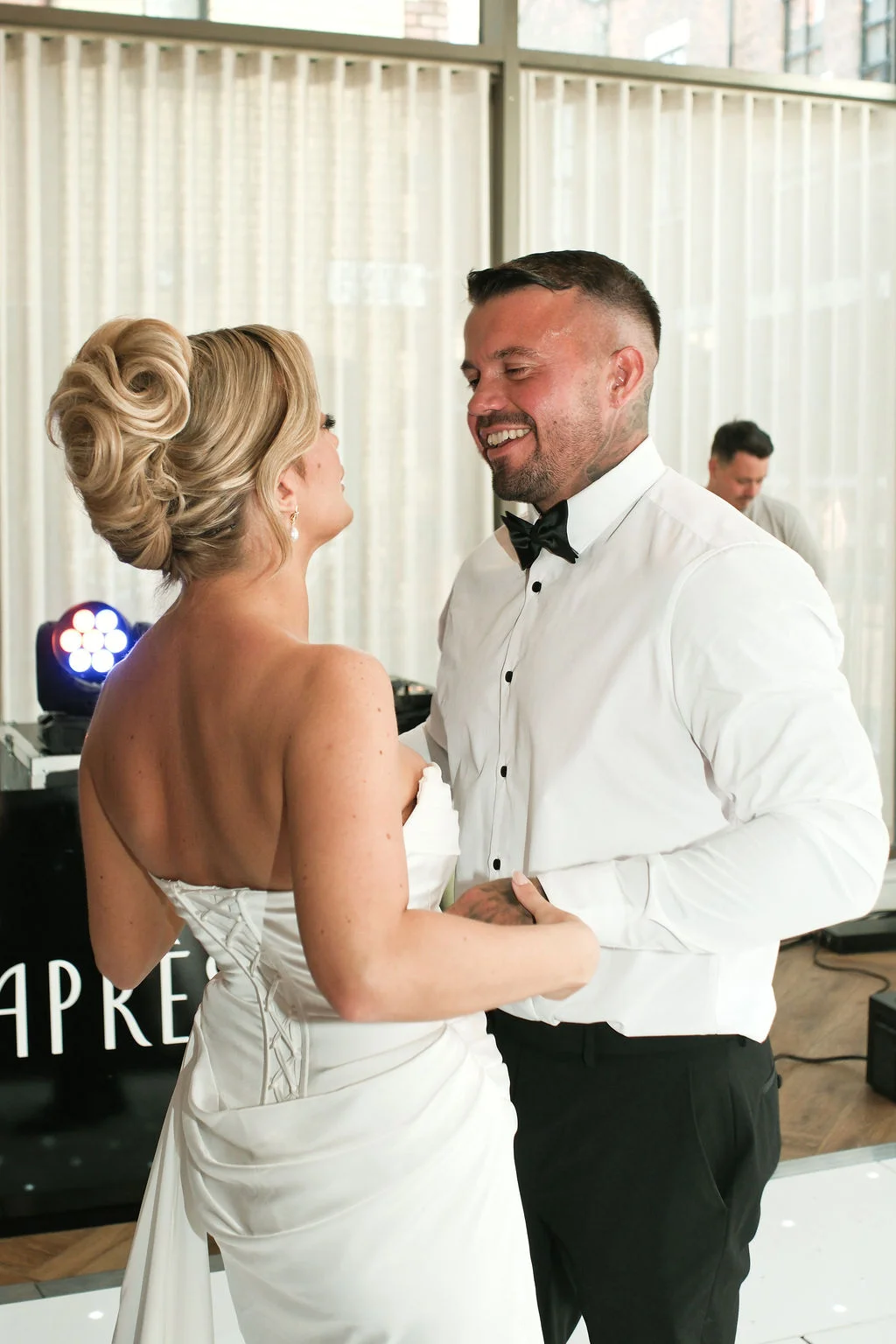 The bride and groom share a joyful moment dancing together indoors during their wedding reception.