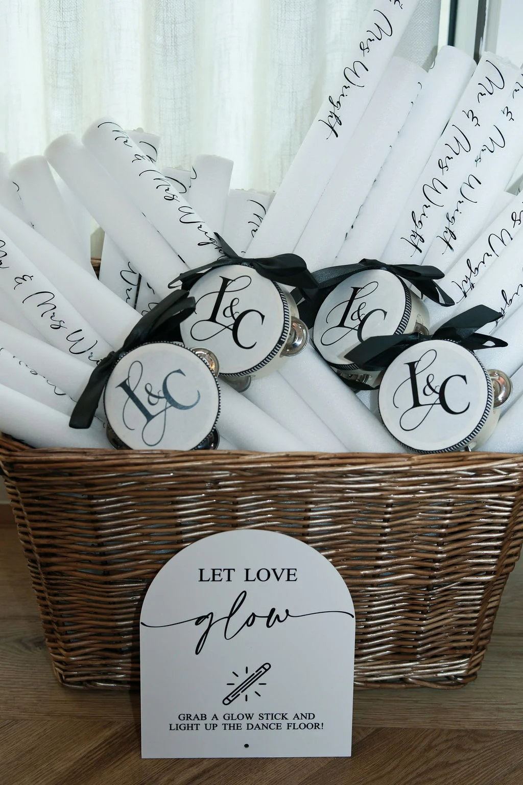 A wicker basket filled with personalised glow sticks and tambourines features an arched sign reading let love glow for guests on the dance floor.