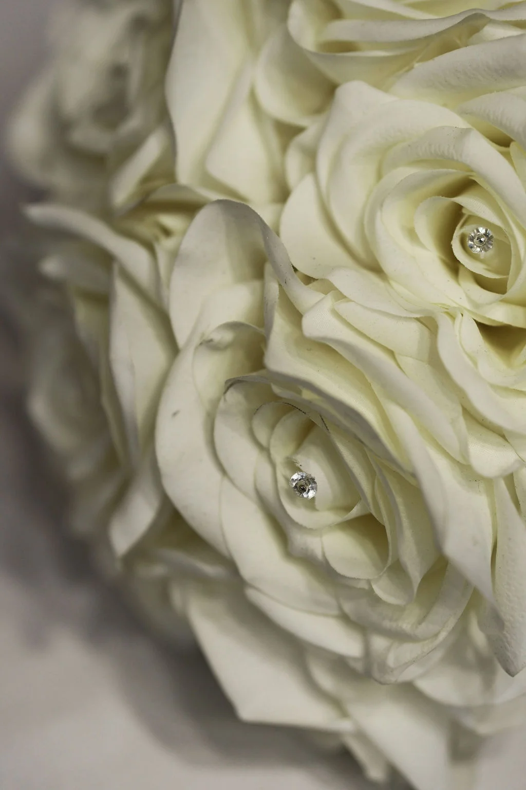 A close up macro shot of a white rose wedding bouquet featuring delicate sparkling crystal pins nestled within the flower centres.