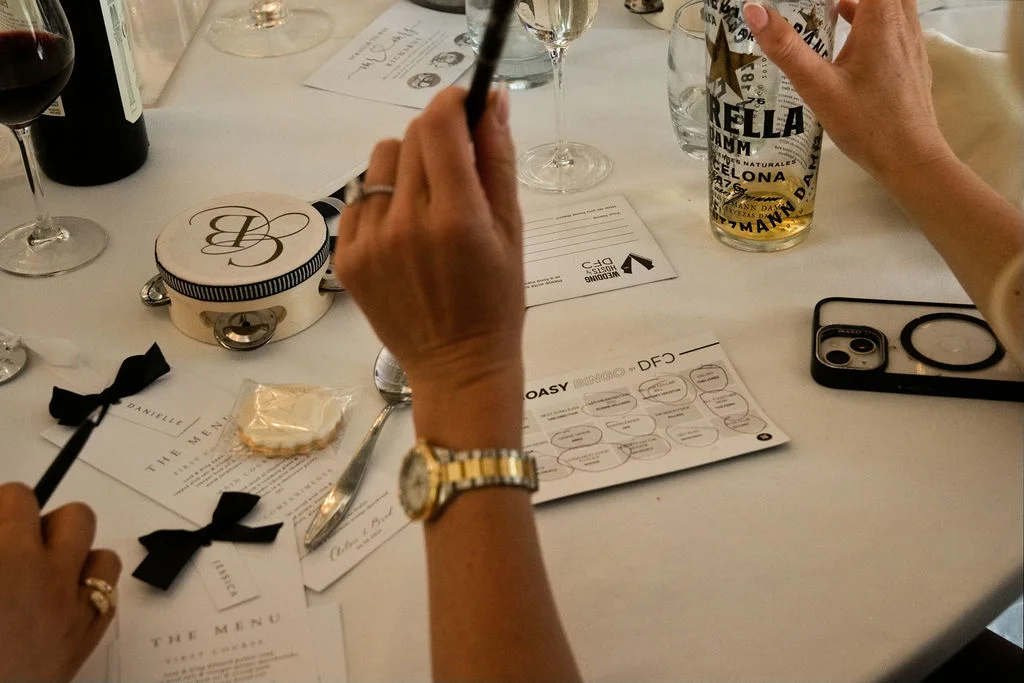 A candid overhead shot of wedding guests interacting at a reception table with menus, place cards, and drinks during the wedding breakfast.