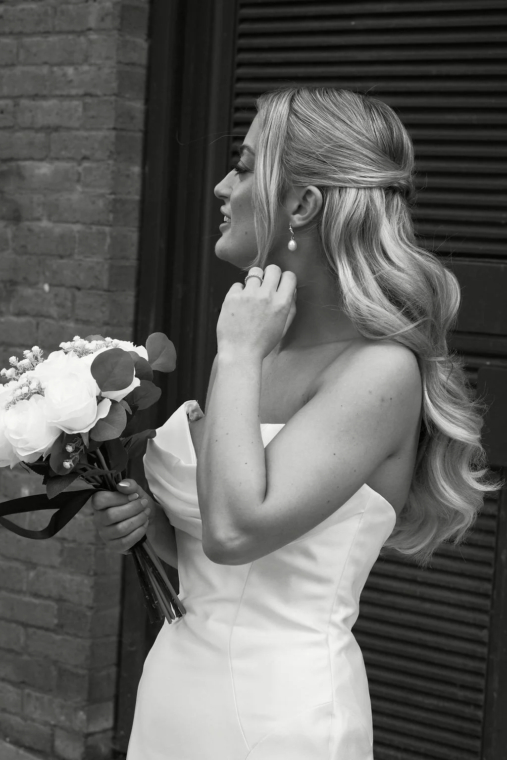 A stunning black and white portrait of a bride in a strapless satin gown holding a white rose bouquet while wearing her hair in a half up half down style.
