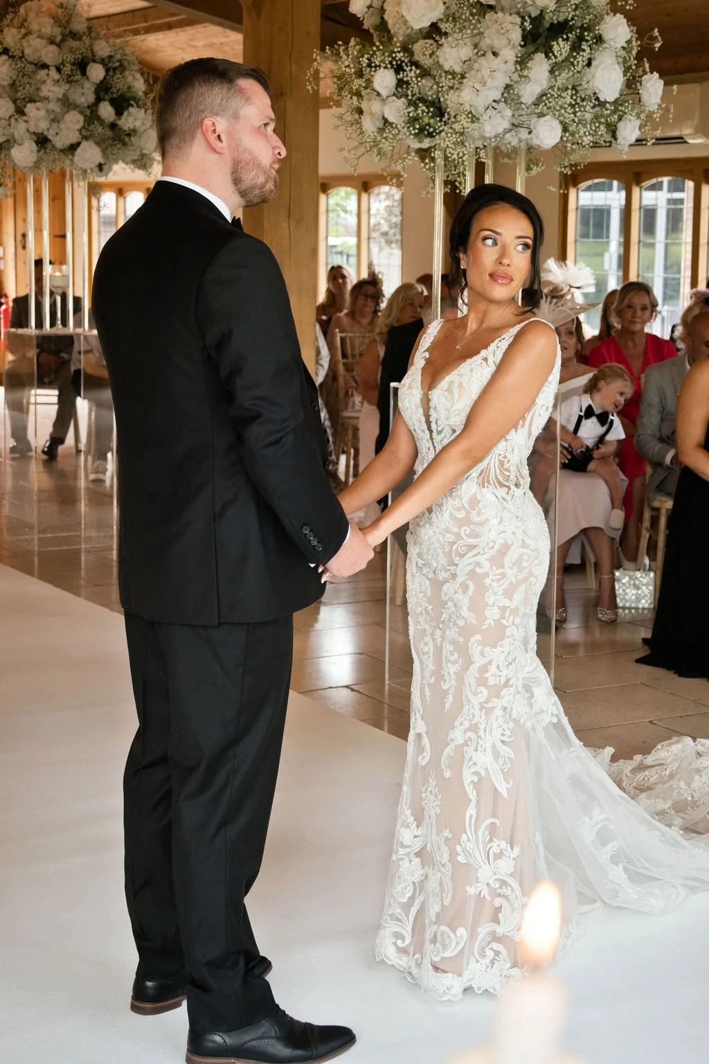 A bride and groom hold hands at the altar during their indoor civil ceremony inside a light-filled barn venue.