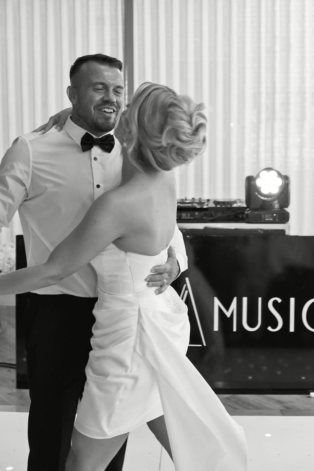 A newlywed couple shares a joyful first dance together near a DJ booth during their wedding reception.