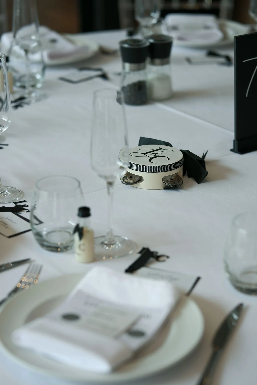 A close-up view of a modern monochrome wedding reception tablescape featuring crisp white linens, minimalist stationery, and elegant black details.
