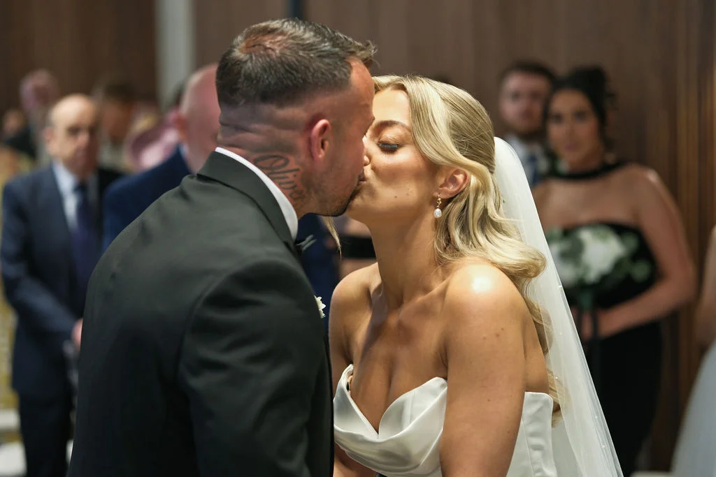A newlywed couple shares their first kiss at the altar during their ceremony, surrounded by family and guests.