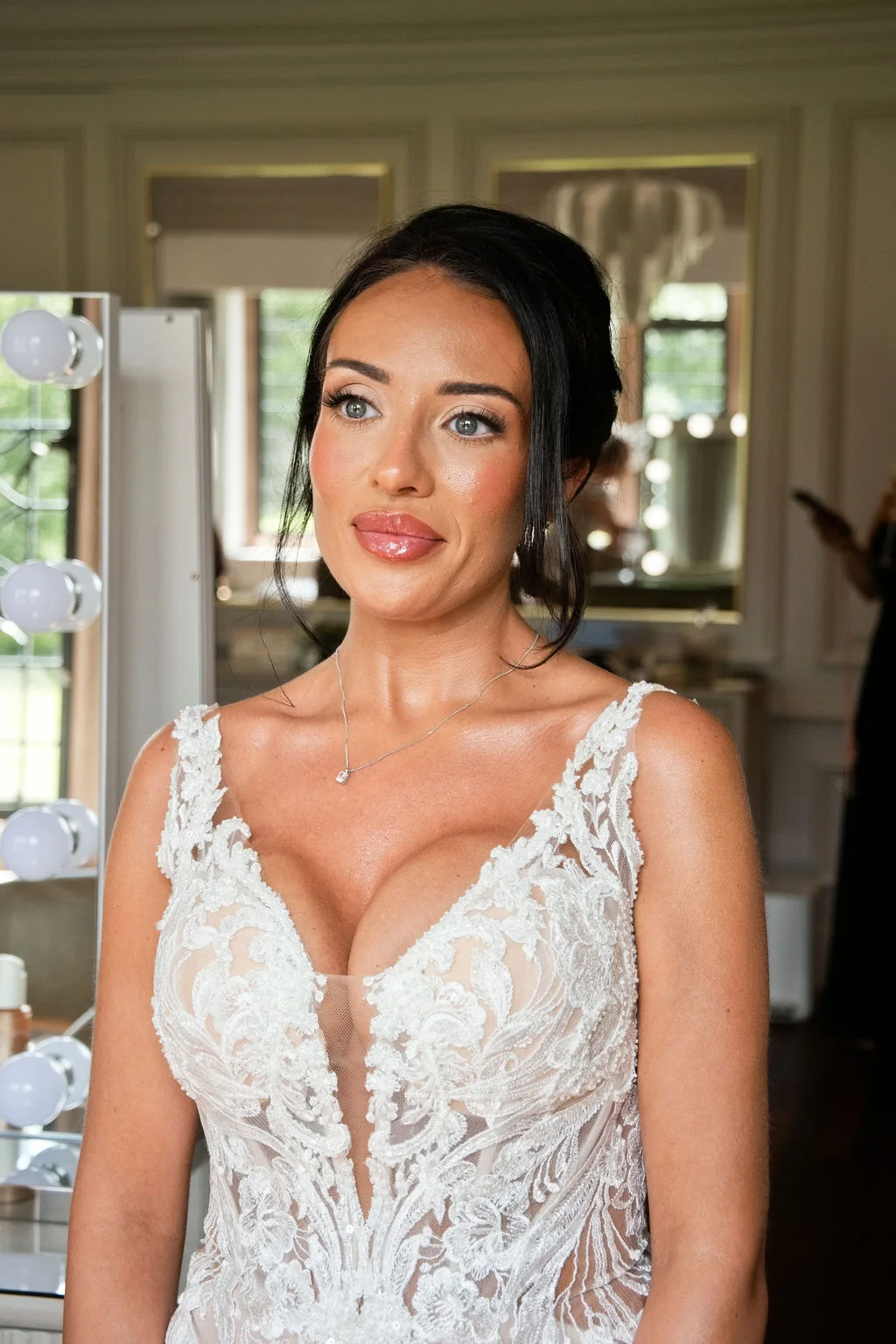 A stunning bride looking off to the side during morning preparations, wearing an intricate lace gown with a plunging neckline and elegant updo.