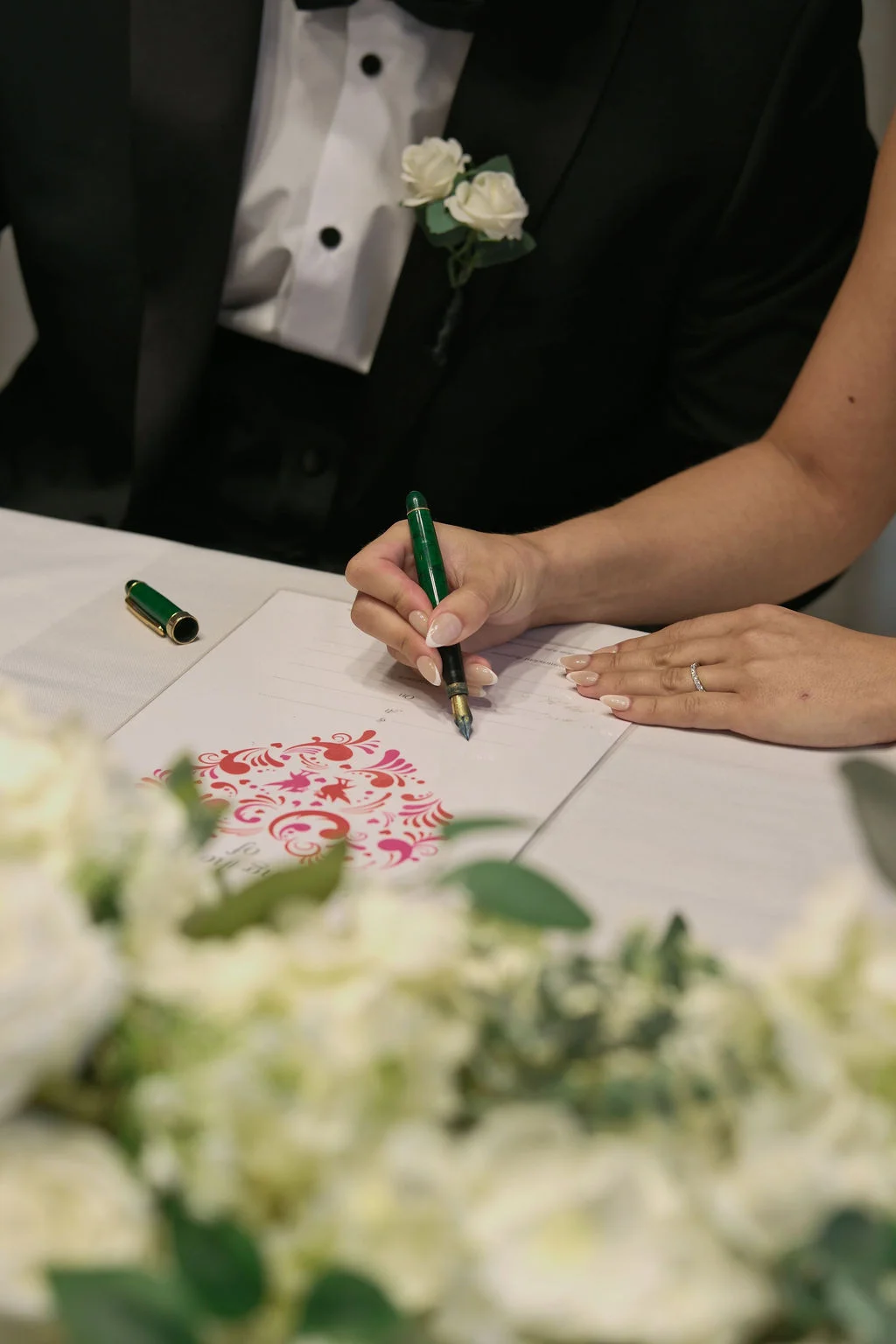 A close-up shot of a bride and groom signing the wedding certificate at a table adorned with white floral arrangements.