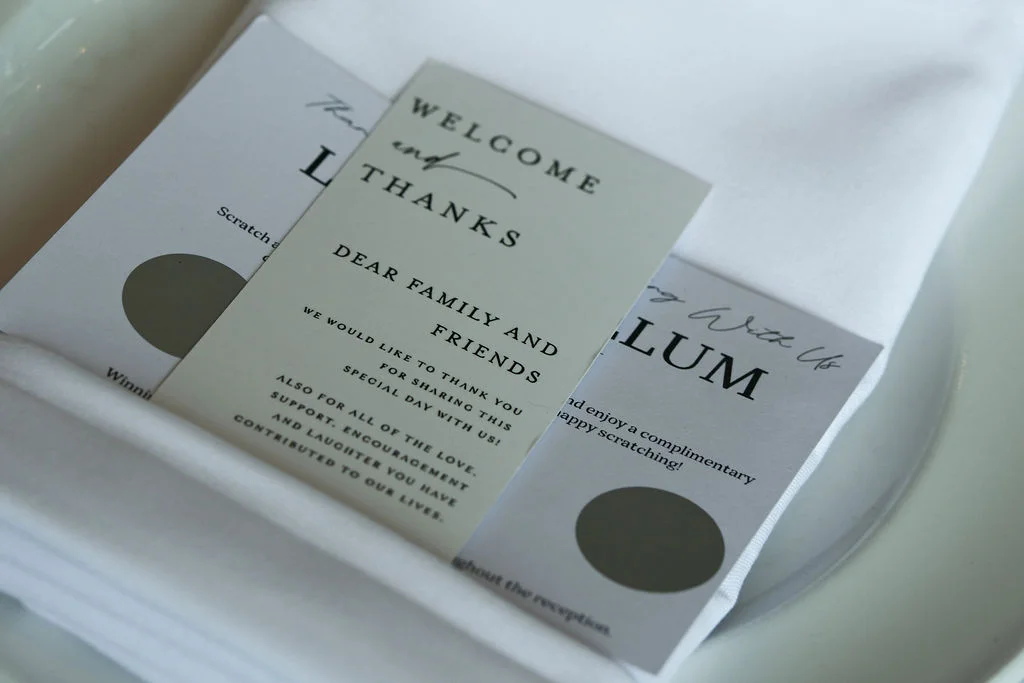 A close-up flat lay showcases modern minimalist wedding stationery and welcome cards resting neatly on folded white linen napkins.