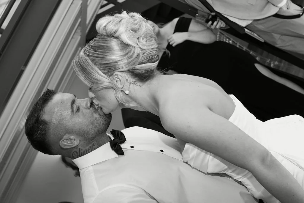 A newlywed couple shares a romantic dip kiss on the dance floor captured in a striking black and white photograph.
