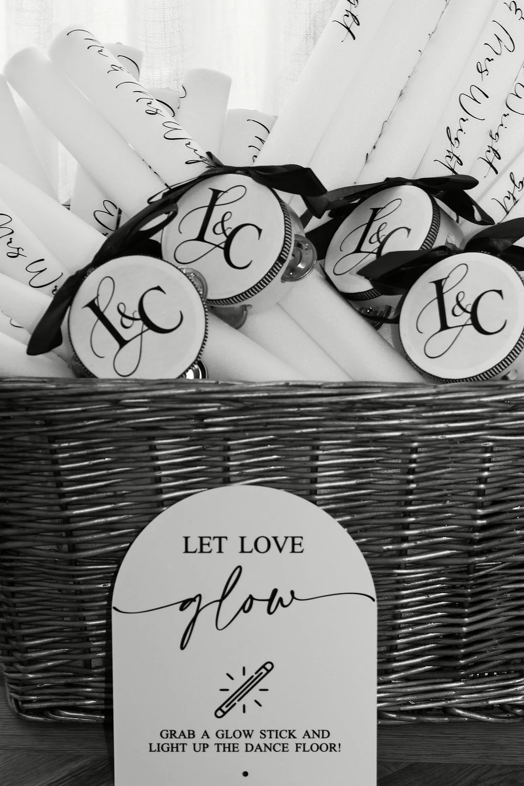 A wicker basket filled with personalised glow sticks features an arched sign reading let love glow for evening guests.