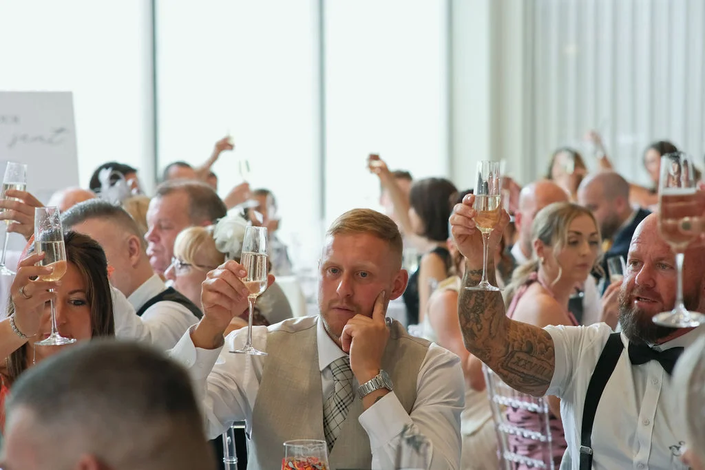 Wedding guests raise champagne flutes in a toast during the speeches at a reception.